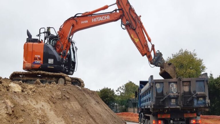 Transport terrassement Genève : une pelle hydraulique charge des déblais dans un camion benne pour l’évacuation de terre sur un chantier à Genève