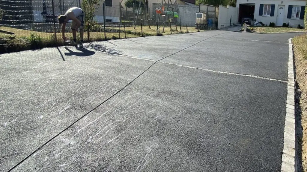Allée de garage en enrobé fraîchement posée à Genève, avec un ouvrier ajustant les finitions le long de la clôture.