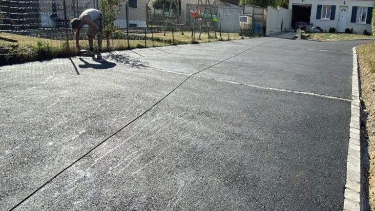 All&eacute;e de garage en enrob&eacute; fra&icirc;chement pos&eacute;e &agrave; Gen&egrave;ve, avec un ouvrier ajustant les finitions le long de la cl&ocirc;ture.