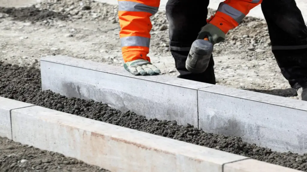 Pose de bordure en béton sur trottoir à Genève par un ouvrier en tenue de sécurité – chantier de réfection voirie conforme aux normes communale