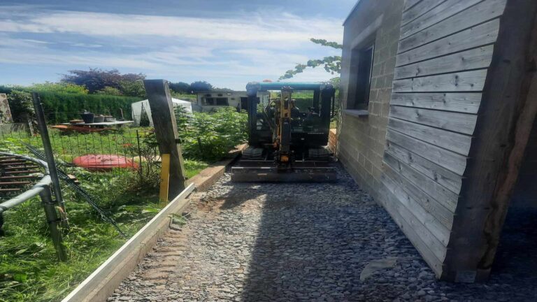 Mini-pelle compacte JD Dusonchet intervenant dans un accès étroit entre deux bâtiments à Genève, démonstration d’un chantier maîtrisé en zone résidentielle dense.